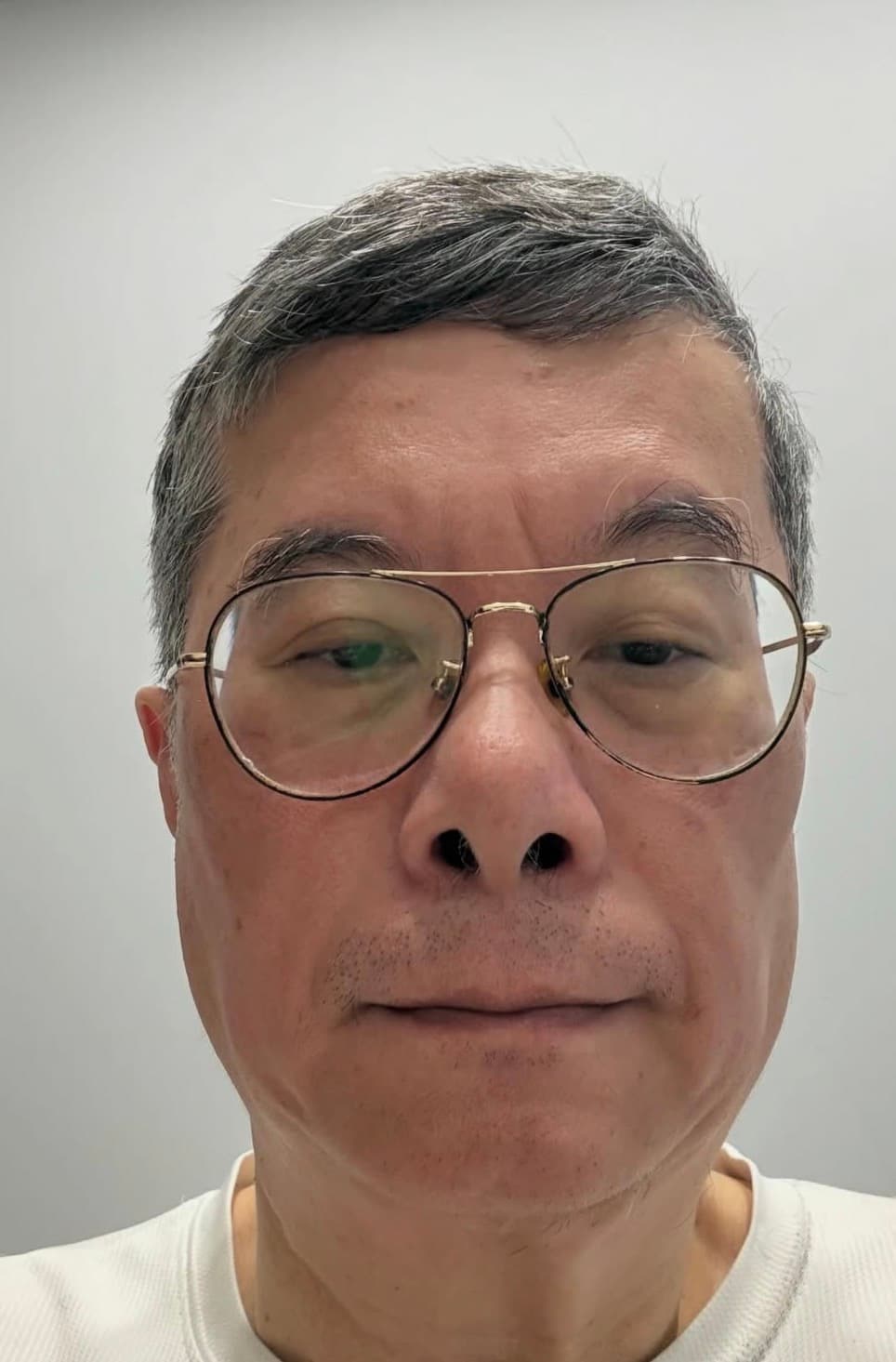 Close-up of an older Asian man with salt-and-pepper hair wearing gold-rimmed aviator glasses.