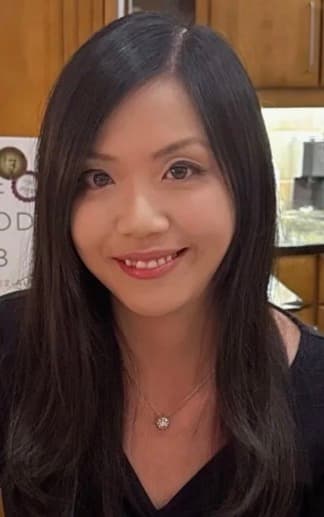 Smiling woman with long dark hair wearing a black top and a delicate pendant necklace.